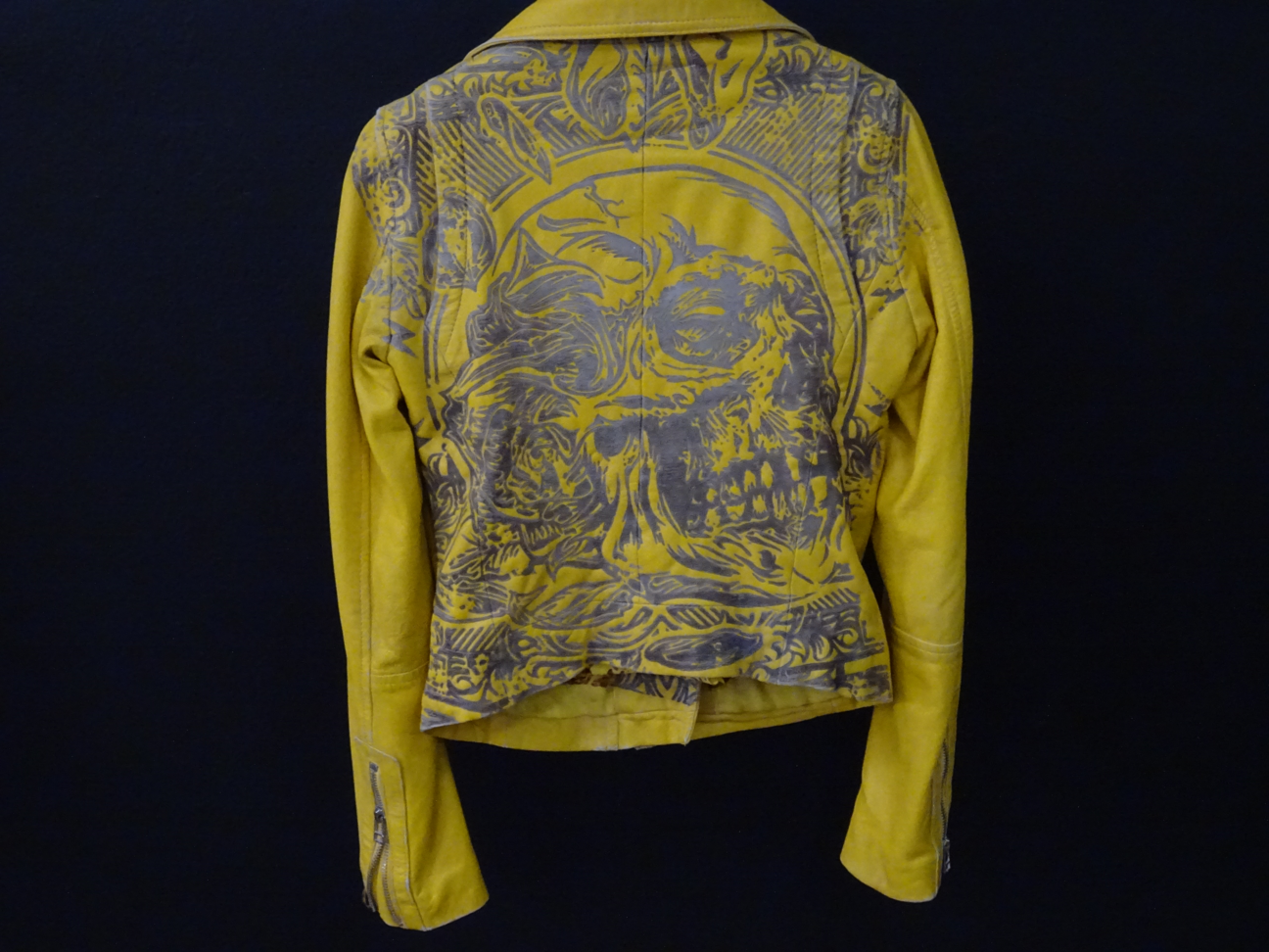 Giacca in pelle gialla con un&apos;incisione laser di un teschio stilizzato sul retro, perfetta per uno stile audace e moderno.  L&apos;immagine mostra una giacca in pelle gialla dal design unico, caratterizzata da una dettagliata incisione laser sul retro che raffigura un teschio stilizzato con motivi artistici. Questo capo fashion combina eleganza e grinta, esaltando la texture della pelle attraverso un processo di personalizzazione sofisticato. Ideale per chi cerca un look distintivo nel mondo della moda urbana, questa giacca incarna lo spirito della customizzazione dei capi in pelle, dove ogni incisione racconta una storia di artigianalità e stile senza tempo. Perfetta per outfit streetwear, biker o casual chic, è l&apos;elemento di tendenza che unisce qualità, carattere e innovazione nel settore fashion.
